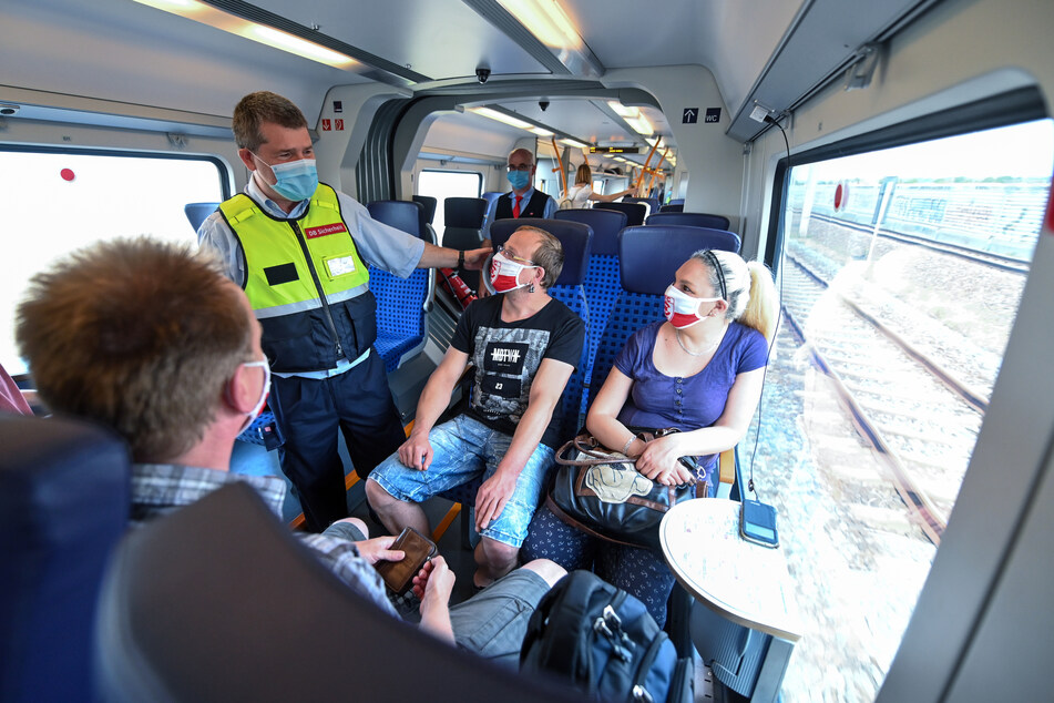 Lutz Fuge (l.) vom Präventionsteam der Deutschen Bahn kontrolliert in einem Regionalzug zwischen Leipzig und Halle das Tragen von Mund-Nasen-Bedeckungen bei den Fahrgästen.