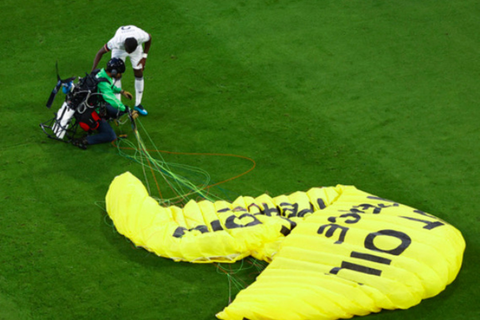 Antonio Rüdiger (Deutschland) spricht mit dem Greenpeace-Aktivist auf dem Spielfeld.