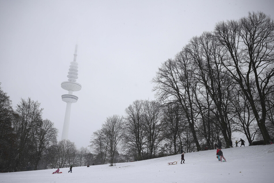 Kinder sind bei Schnee mit ihren Schlitten im Schanzenpark unterwegs.