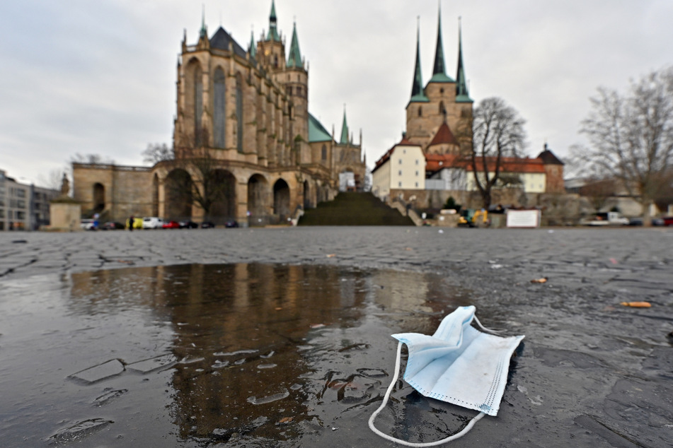 Ein Mund-Nasen-Schutz liegt auf dem Domplatz in Erfurt in einer Pfütze. Thüringen hat derzeit bundesweit die niedrigste Inzidenz.