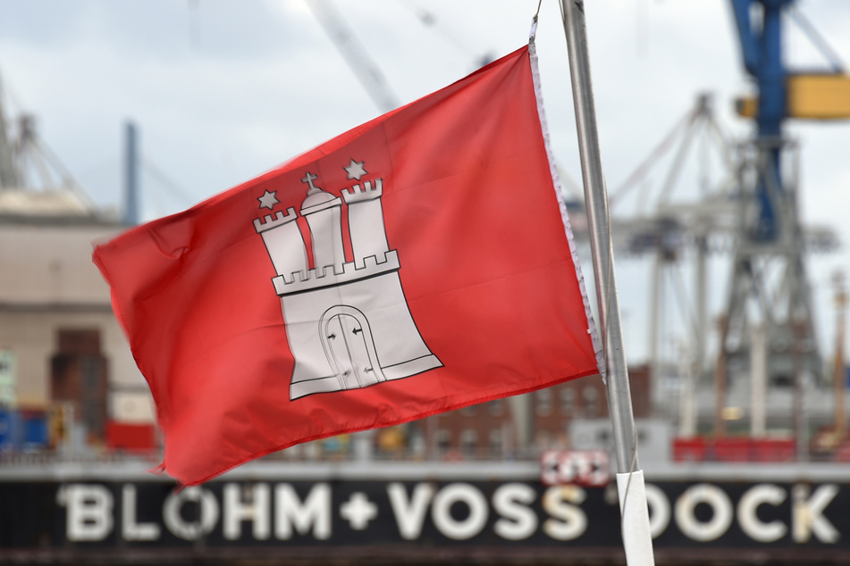 Eine Hamburg-Flagge weht auf einer Fähre im Hafen vor einem Trockendock der Werft Blohm+Voss.