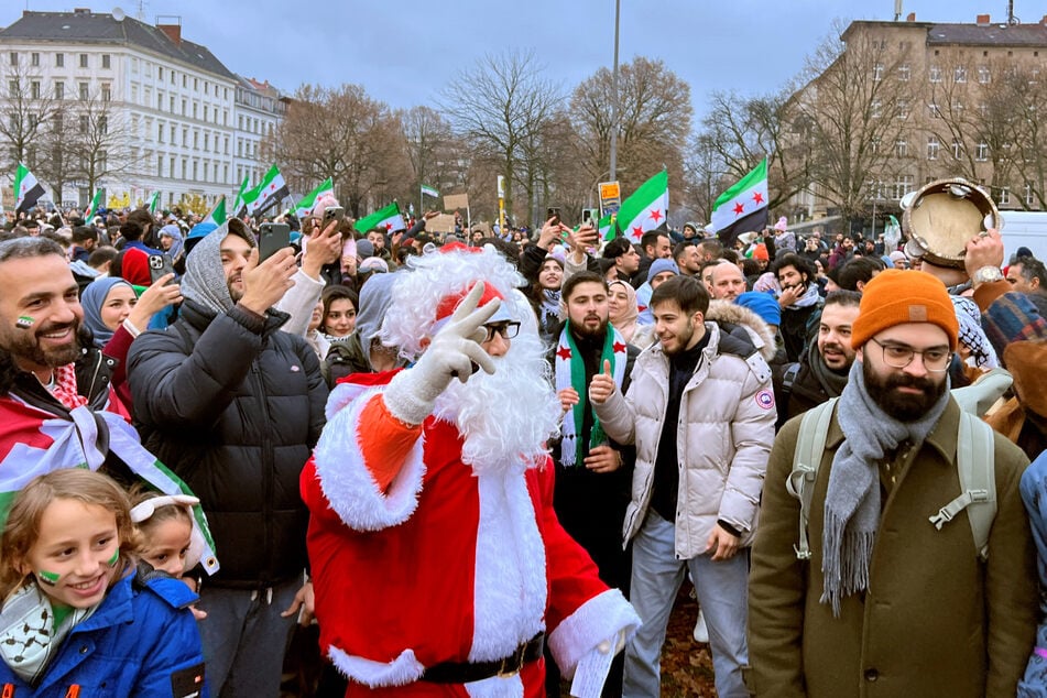 Menschen und ein als Weihnachtsmann verkleideter Mann feiern auf dem Oranienplatz in Kruezberg den Sturz des Assad-Regimes.