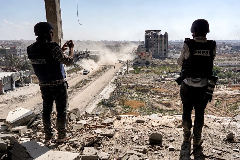 Palestinian journalists film from atop a damaged building facing the ravaged building of Al-Salam hospital in Khan Younis.