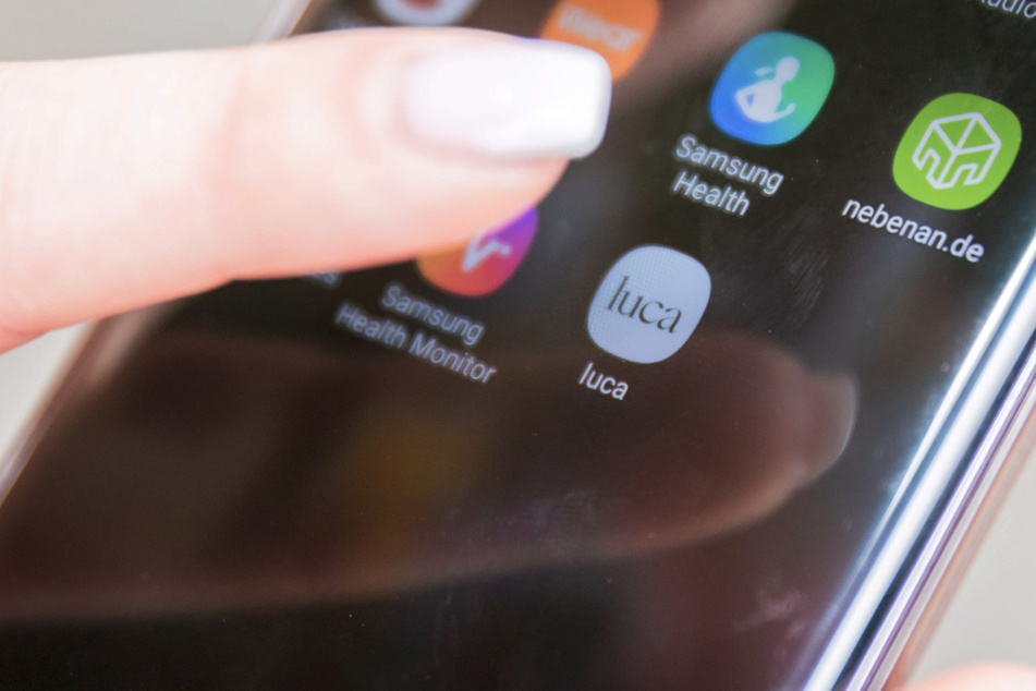 Eine Kundin hält am Eingang eines Bekleidungsgeschäftes am Alexanderplatz ein Smartphone mit der Luca-App in die Kamera.
