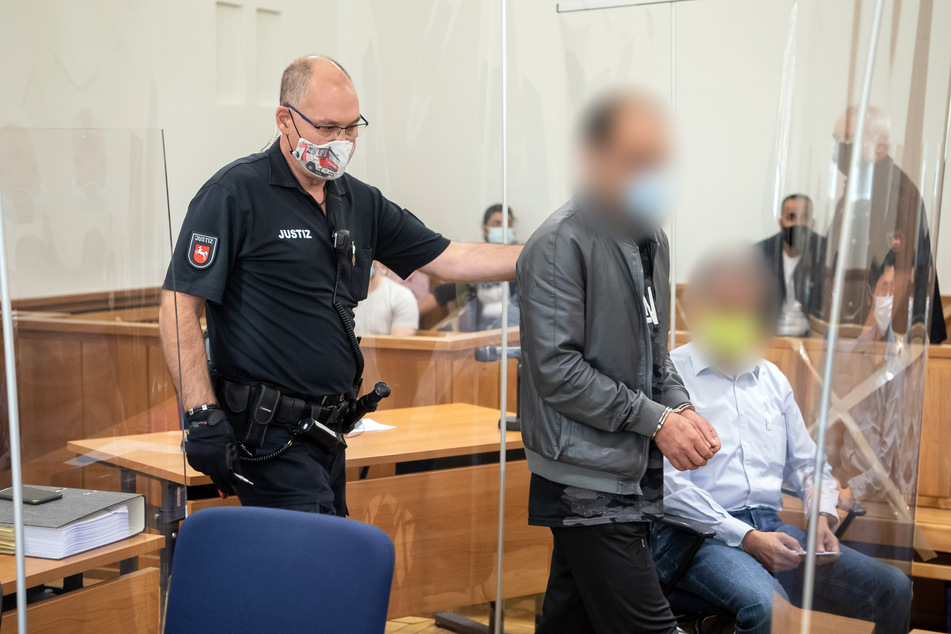 Einer der Angeklagten wird in Handschellen in den Gerichtssaal geführt.