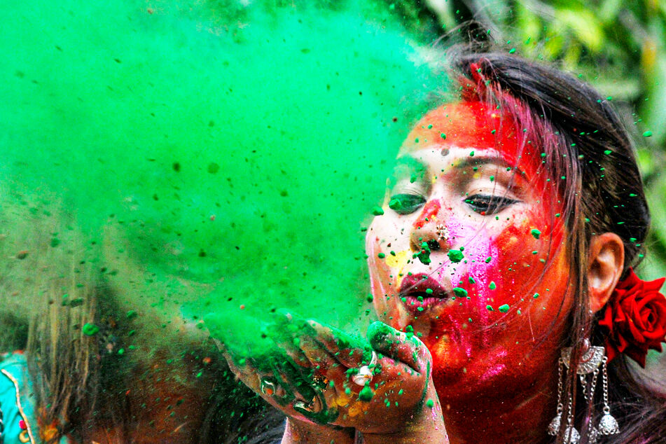 Eine geschminkte Studentin pustet farbiges Pulver von ihren Händen während der Holi-Feierlichkeiten an der Universität Kalkutta, Indien.