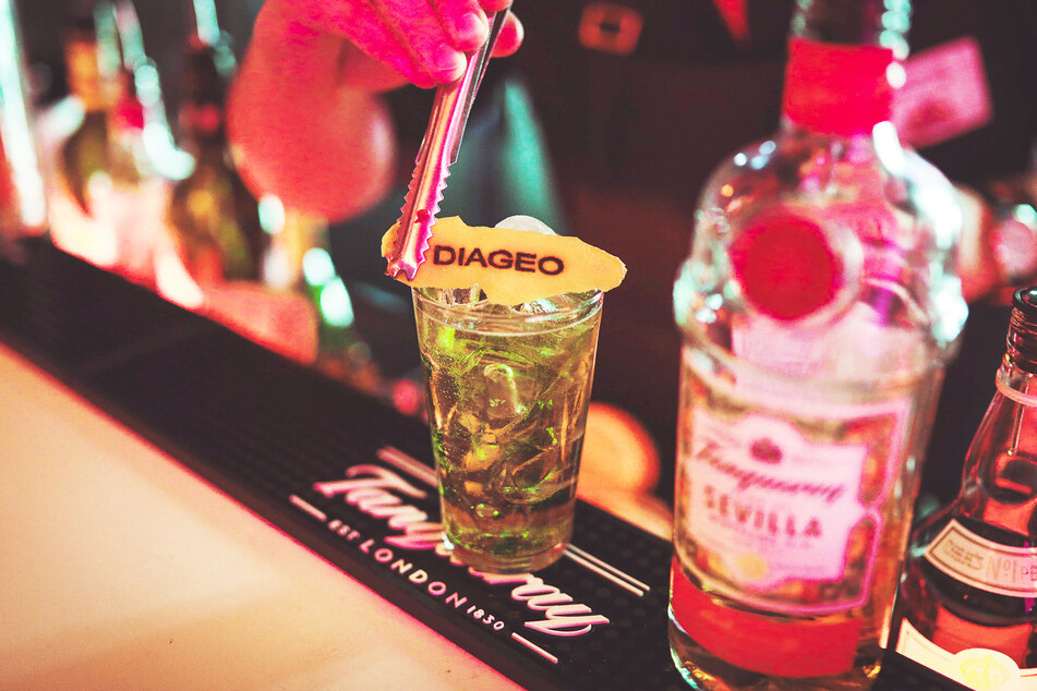 Ein Barkeeper mixt einen Tanqueray-Gin mit Tonic und richtet das Getränk mit einem Stück Zitronenschale an, auf dem "Diageo" steht.
