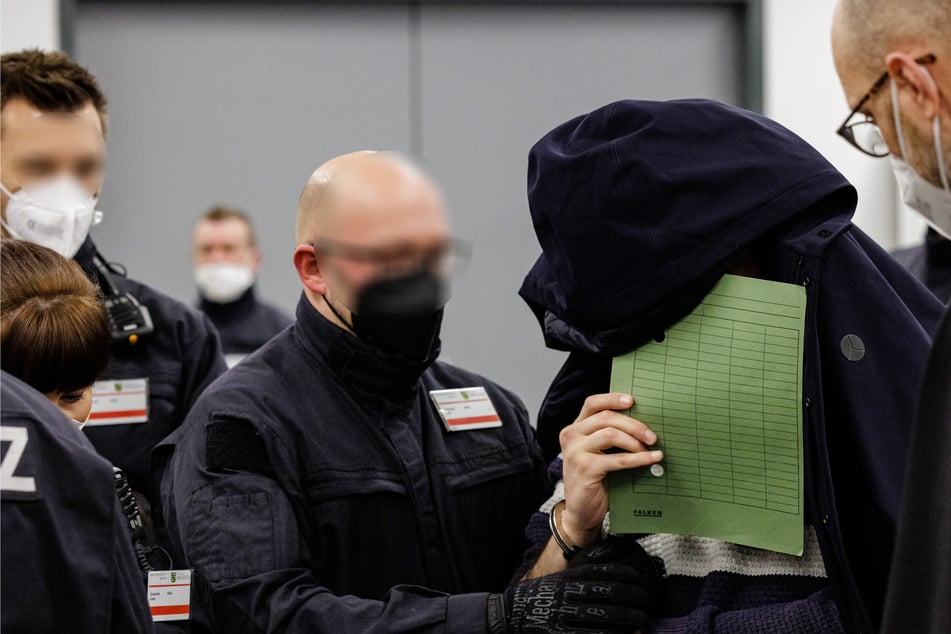 One of the accused covers his face while being led into a hall of the Dresden Higher Regional Court.