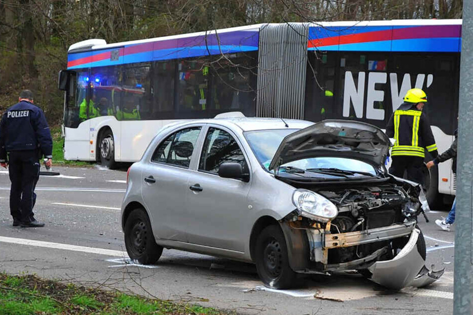 Ein Polizist steht an einer Unfallstelle hinter einem stark beschädigtem PKW und vor einem Bus.