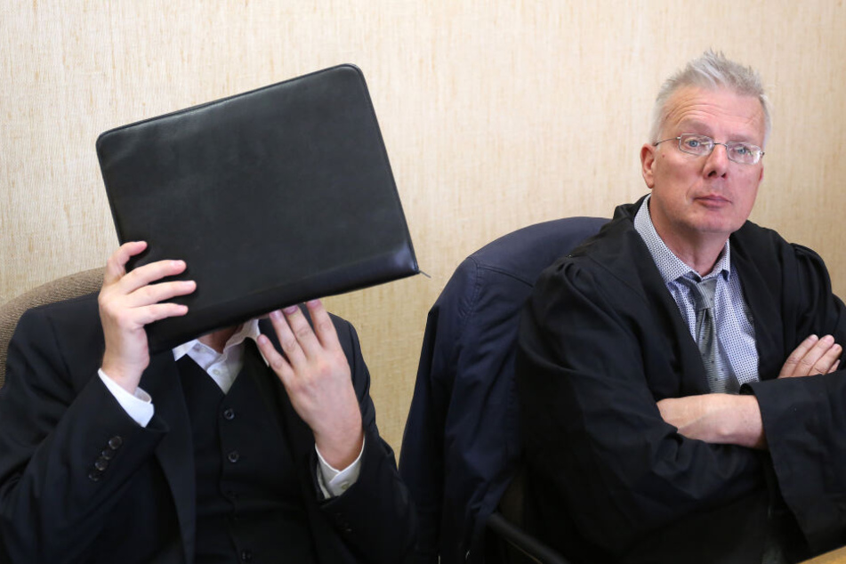Der Angeklagte hält sich im Amtsgericht neben seinem Anwalt Konrad Schäfer (r) eine Aktentasche vor das Gesicht.