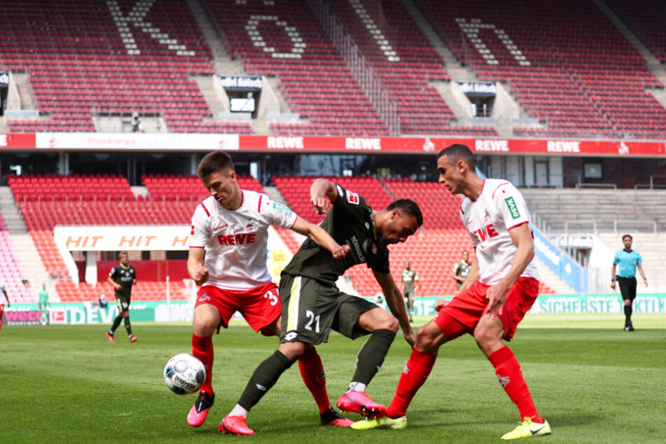 Noah Katterbach (l.) und Ellyes Skhiri (r.) luchsen dem auffälligen Mainzer Karim Onisiwo mit vereinten Kräften und vor gähnend leeren Rängen den Ball ab.