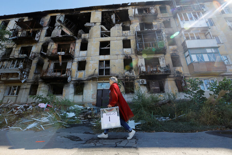 A local election official carries ballots past a damaged residential building in Mariupol.