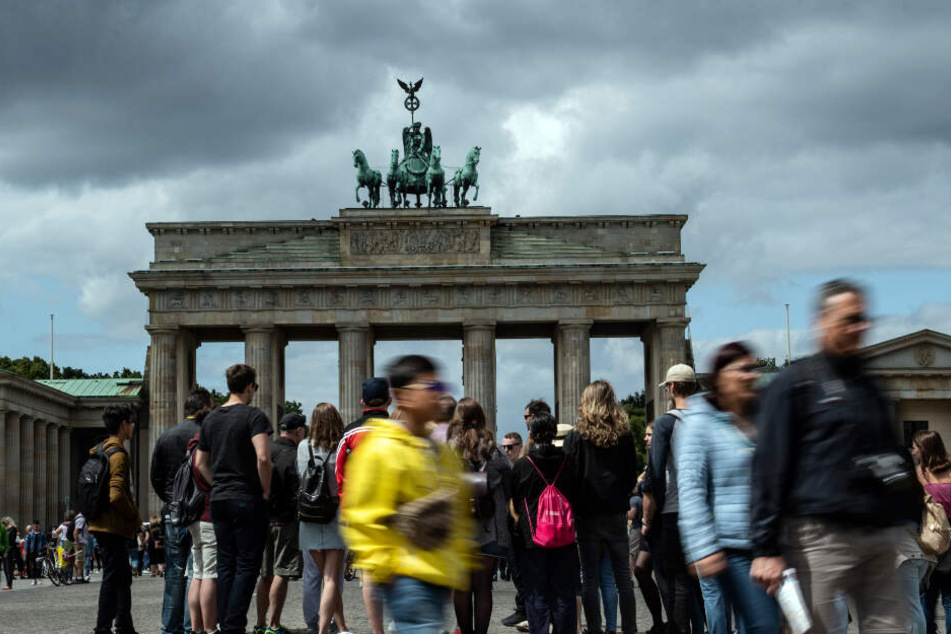 Dunkle Wolken ziehen über das Brandenburger Tor, während zahlreiche Menschen auf dem Pariser Platz stehen.