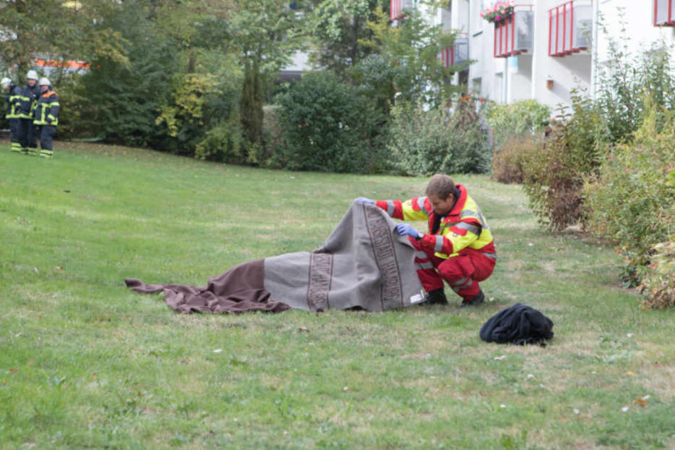 Unter einer Decke der Feuerwehr liegt das 50-jährige Opfer auf dem Rasen.