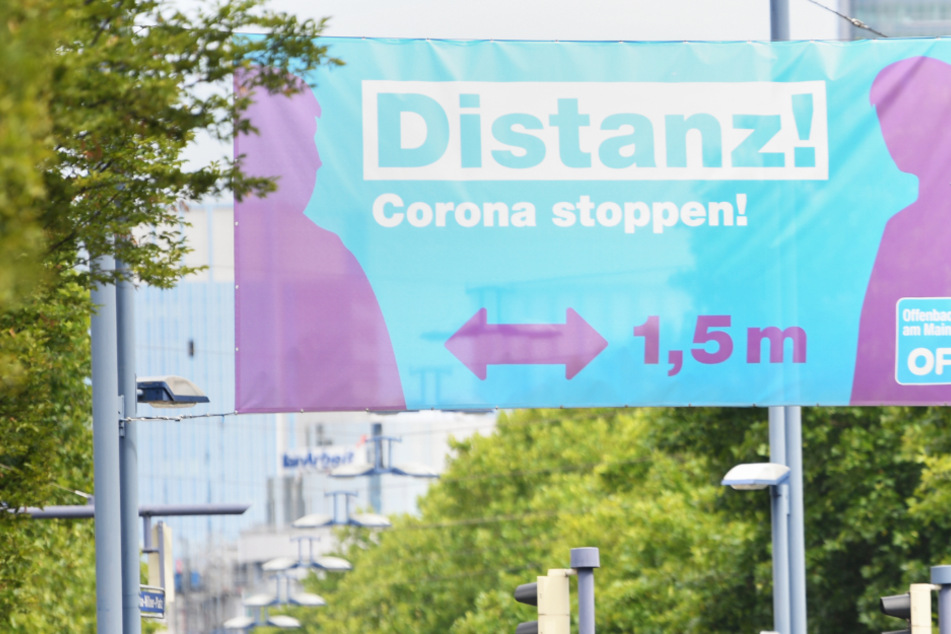 Ein großes Plakat mit der Aufschrift "Distanz! Corona stoppen!" prangt am Ortseingang von Offenbach.