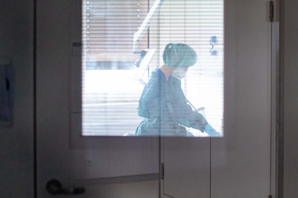 Eine Krankenschwester auf der Infektionsstation der Uniklinik Essen versorgt in Schutzkleidung und mit einer Atemmaske einen Patienten.