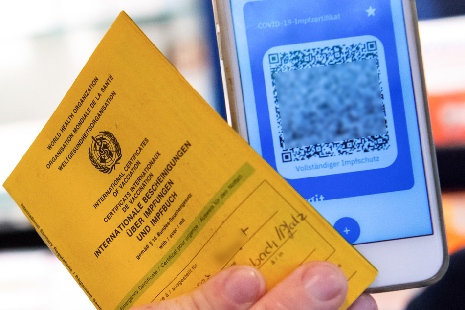 Bayern, München: Ein Apotheker hält einen Impfpass und einen digitalen Impfnachweis in den Händen.
