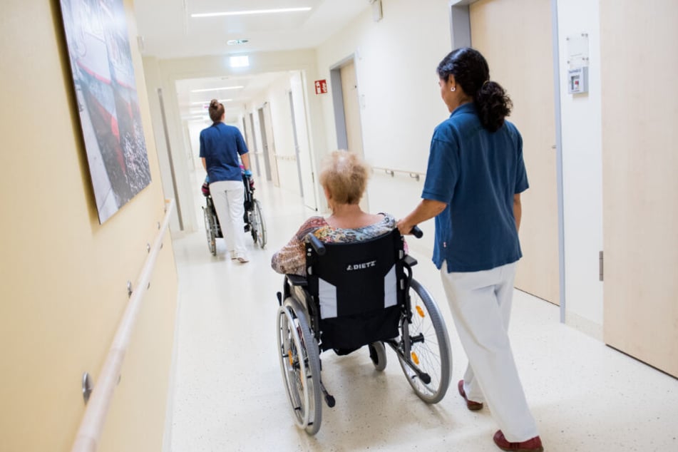 Zwei Pflegerinnen schieben in einem Klinikum Patienten mit Rollstühlen durch einen Flur. (Symbolbild)