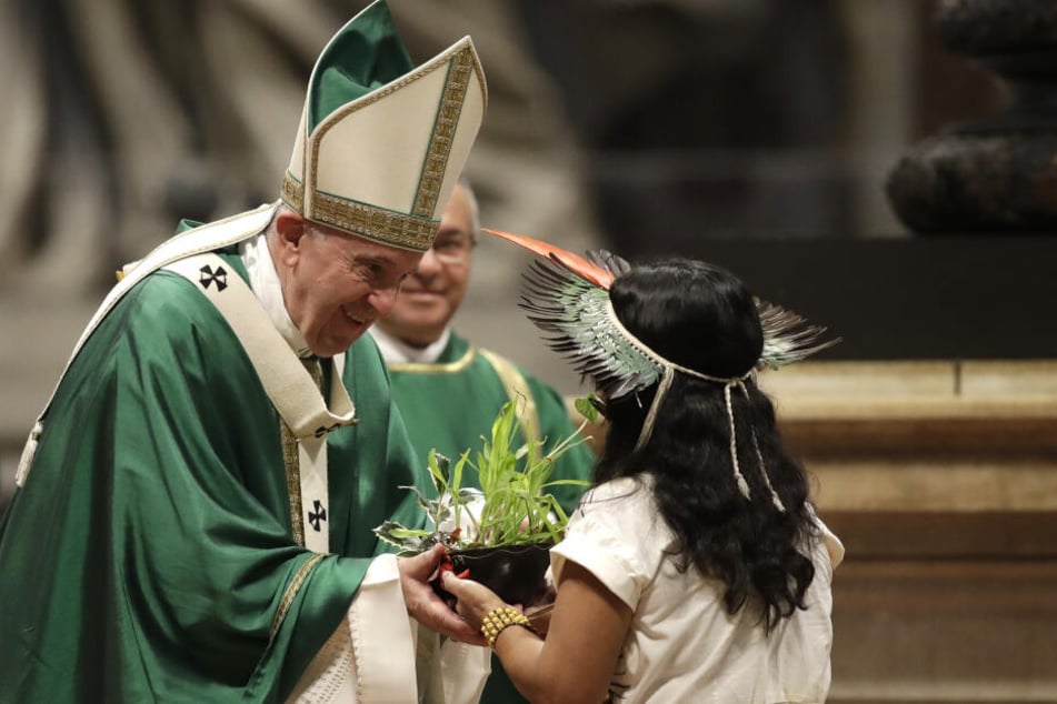Ein Mädchen aus dem Amazonas-Gebiet überreicht Papst Franziskus während Abschluss-Messe der Bischofssynode über die Amazonas-Region eine Pflanze.