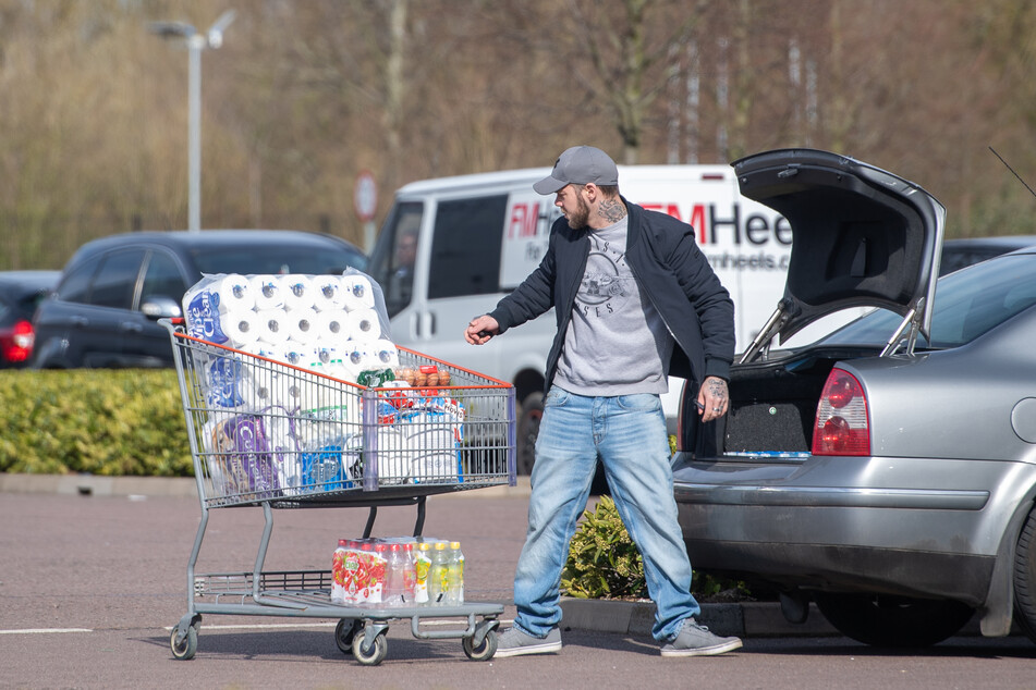Ein Mann lädt auf einem Parkplatz Toilettenpapier in sein Auto.