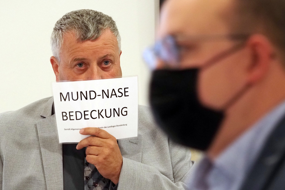 Michael Hanko (AfD) hält sich während der Landtagssitzung ein Schild mit dem Aufdruck "Mund-Nase-Bedeckung" vors Gesicht.
