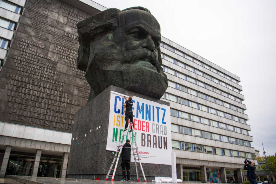 Zwei Männer befestigen am Karl-Marx-Denkmal ein Plakat mit der Aufschrift "Chemnitz ist weder grau noch braun". (Archivfoto)
