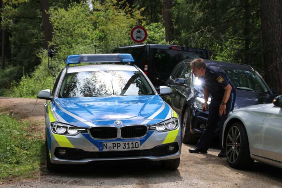 Ein Polizist steht auf einem Waldweg an einem Einsatzfahrzeug der Polizei. In einem Wald im Landkreis Nürnberger Land ist ein toter Mann gefunden worden. Die Kriminalpolizei hat die Ermittlungen aufgenommen.