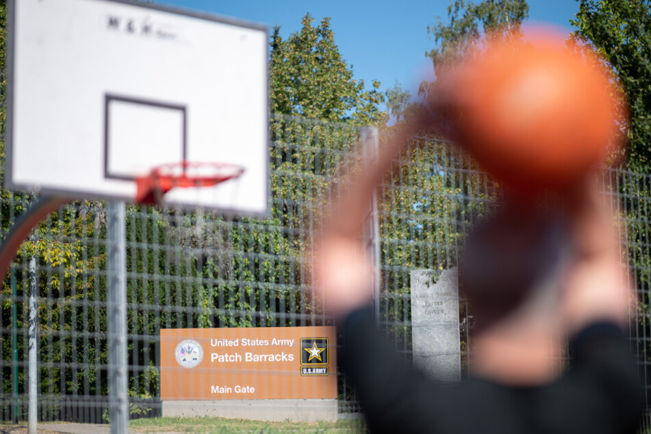 Ein Mann spielt vor einem Schild, das auf den Haupteingang der US-Kaserne "Patch Barracks" hinweist, Basketball.