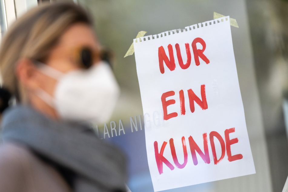 Mit Mund-Nasen-Schutz geht eine Frau an einem Geschäft vorbei.