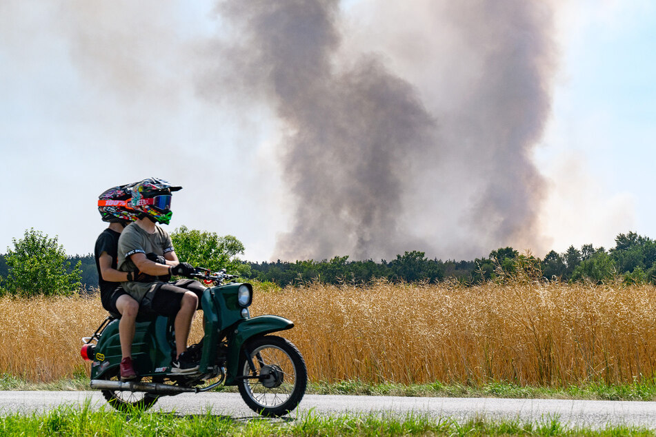 Zwei Männer fahren am Nachmittag auf ihrer Schwalbe an dem Großbrand vorbei.