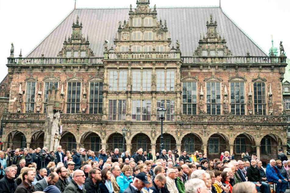 Bei der Wahlkampfveranstaltung der CDU sitzen viele Menschen auf dem Marktplatz vor dem alten Rathaus in Bremen.