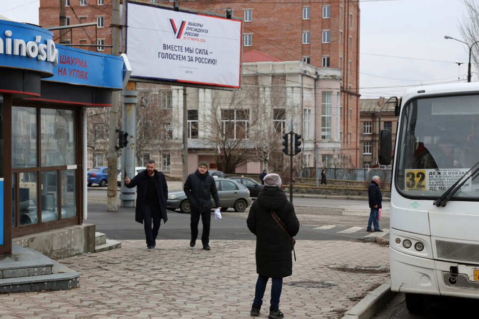 Fußgänger gehen in Donezk in der Ostukraine an einer Plakatwand vorbei, die für die bevorstehenden Präsidentschaftswahlen in Russland wirbt.