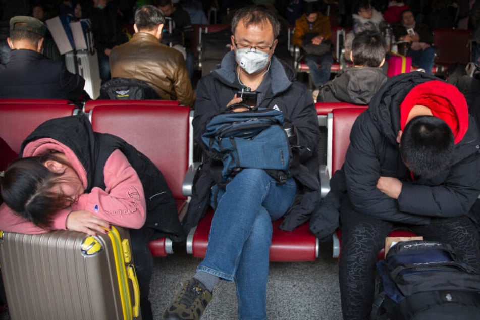 Reisende tragen als Schutzmaßnahme gegen die Verbreitung des Corona-Virus Mundschutz, während sie in einem Wartezimmer am Pekinger Westbahnhof sitzen.