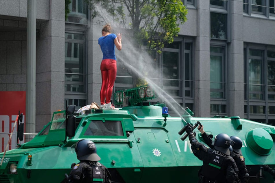 Eine junge Frau klettert auf ein Einsatzfahrzeug der Polizei und bekommt eine Ladung Pfefferspray ins Gesicht.