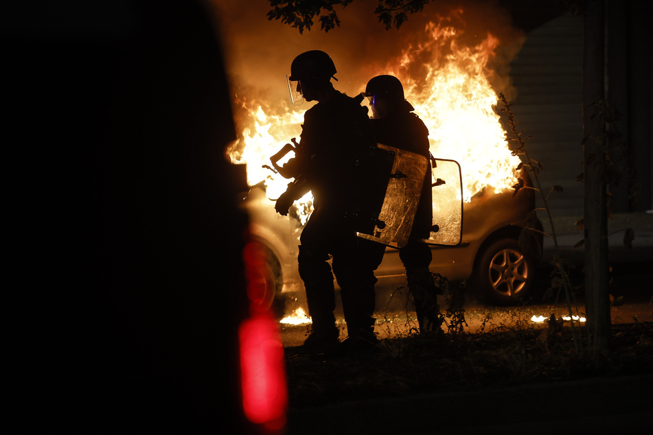 Polizisten in Straßburg stehen vor einem Auto in Flammen.