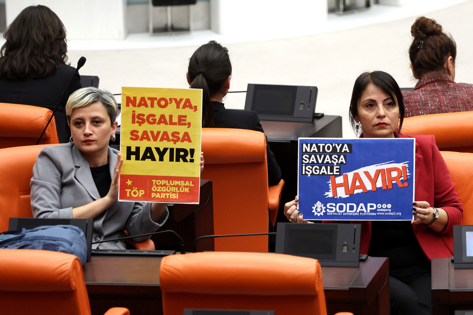 Perihan Koca (l) and Kezban Konukcu held signs reading "No to NATO, Occupation, War" during voting on a bill regarding Sweden's accession to NATO.