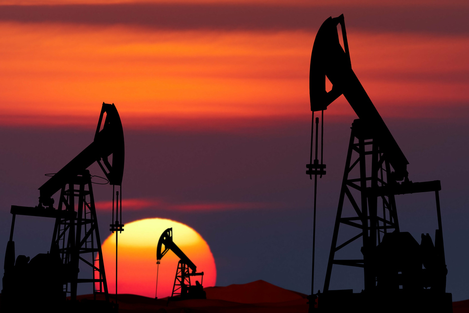 Oil pump jacks at sunset, they enjoy long walks on the beach and environmental destruction (stock image)