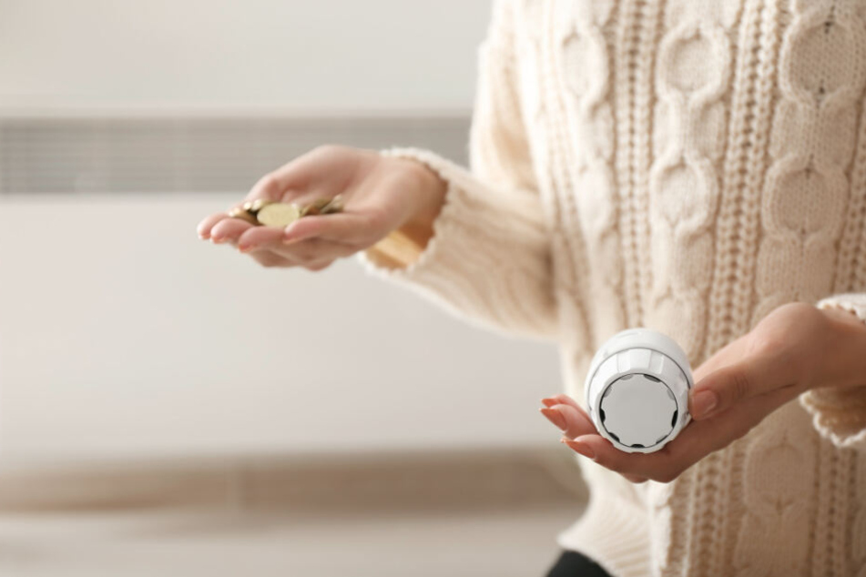 Eine Frau hält ein Heizungsthermostat in der Hand.