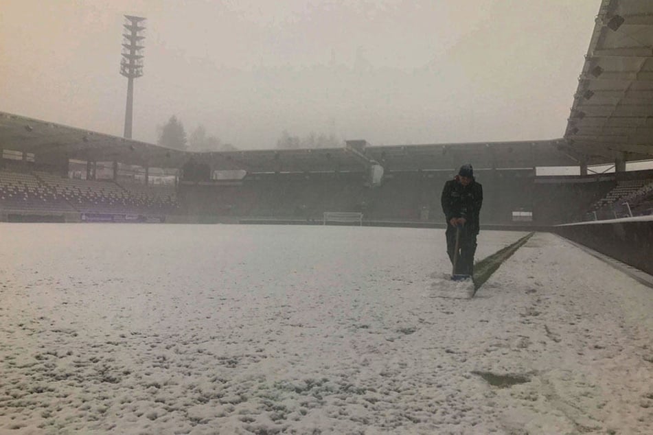 Ein Stadionarbeiter beräumt mit dem Schneeschieber die Außenlinie - ein aussichtsloser Kampf.