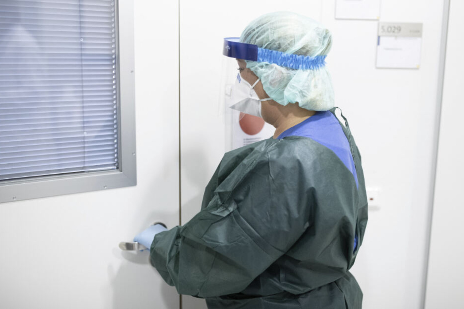 Canan Emcan, Stationsleiterin auf der Infektionsstation der Uniklinik Essen, steht in Schutzkleidung und mit einer Atemmaske in einer Schleuse vor einem Patientenzimmer.
