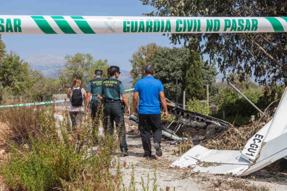 Die Absturzstelle ist mit einem Absperrband der "Guarda Civil" abgesperrt, Mitglieder der Polizeieinheit "Guardia Civil" stehen mit zwei anderen Personen hinter einem Teil des Flugzeugwracks.