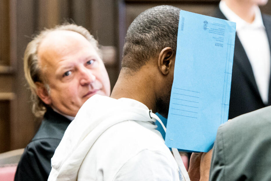 Der Angeklagte verbirgt sein Gesicht vor der Presse hinter einem Aktenordner (Archivbild). Neben ihm sitzt sein Anwalt Tim Burkert.