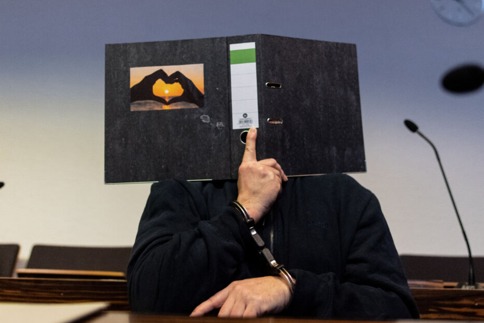 Der 58-Jährige hält sich vor Gericht einen Aktenordner vors Gesicht.