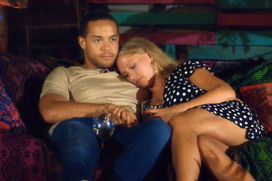 Der Bachelor und die Kandidatin Vanessa halten Händchen auf einem Sofa.