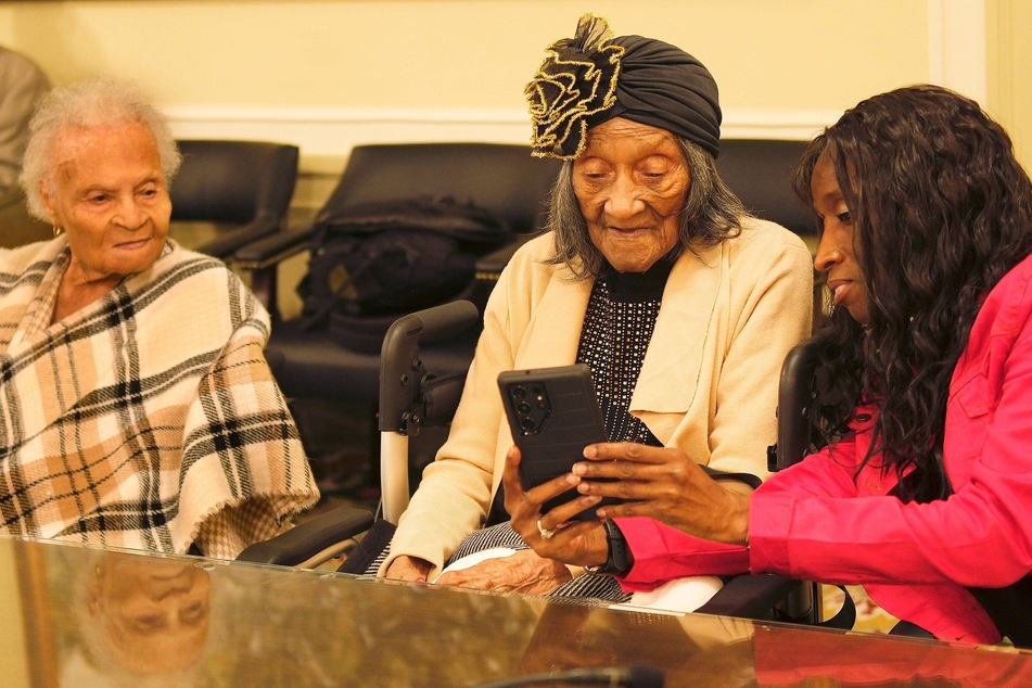 Viola Ford Fletcher (l.) looks on as LaDonna Penny (r.) takes a photo of Lessie Benningfield Randle to post on social media.