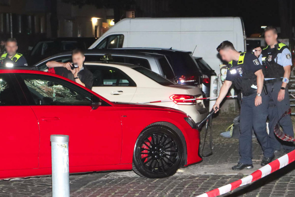 Polizeibeamte dokumentieren die Schäden an der Windschutzscheibe des Audis und rekonstruieren den Tathergang.