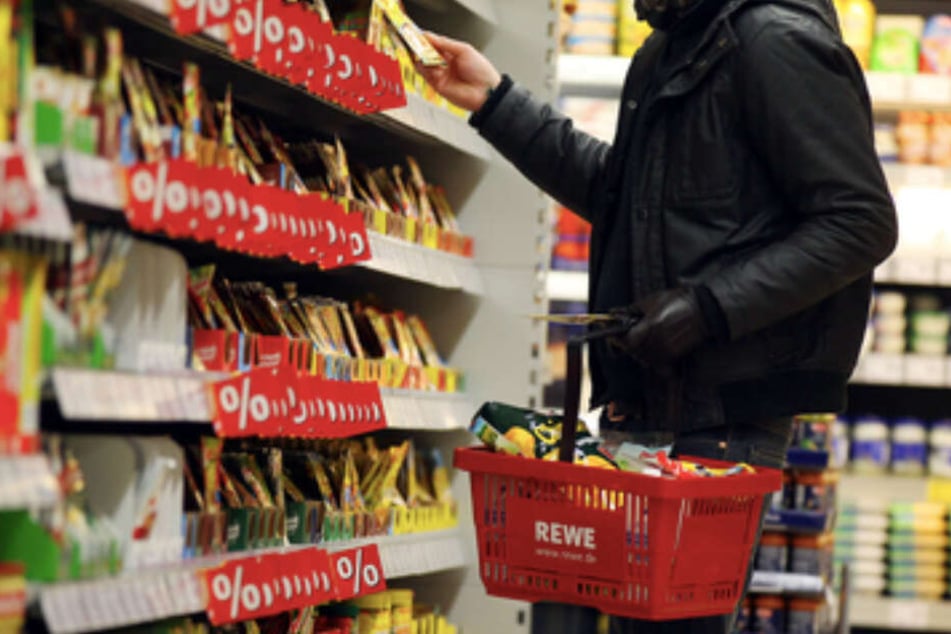 In einem Rewe-Supermarkt steht ein Kunde vor einem Regal (Symbolbild).