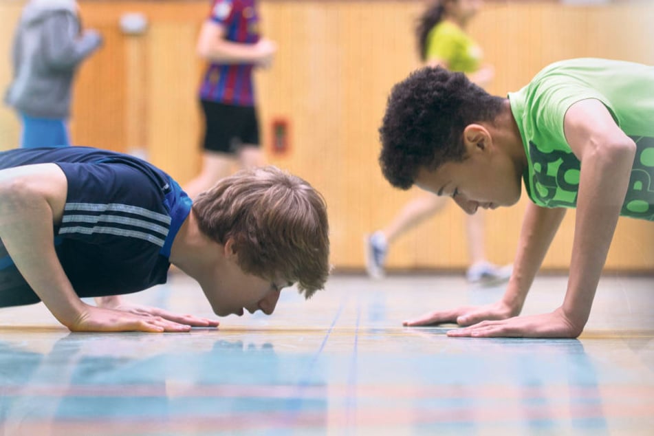 Zwei Jungen machen im Sportunterricht Liegestütze um die Wette. Sie haben dabei gemeinsam viel Spaß am Kräftemessen.