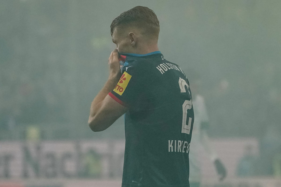 Kiels Mikkel Kirkeskov (30) hält sich im Nordderby im Bremer Pyro-Nebel die Nase zu. Fans des SV Werder Bremen haben insbesondere in der zweiten Halbzeit immer wieder Bengalos gezündet.