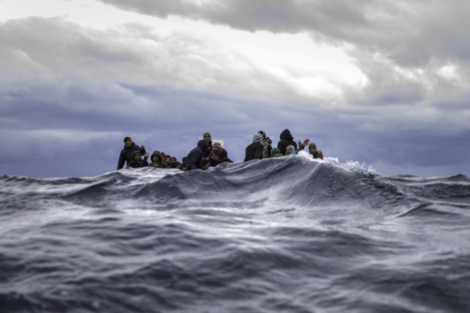 Männer aus Marokko und Bangladesch sitzen in einem überfüllten Holzboot im Mittelmeer vor der Küste von Libyen.